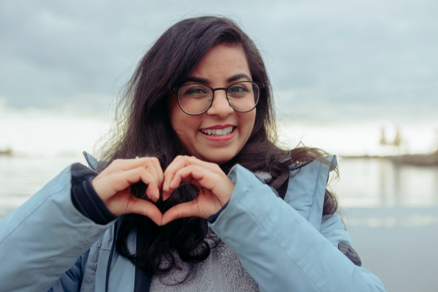 A student making the heart sign with her fingers on a sea shore
