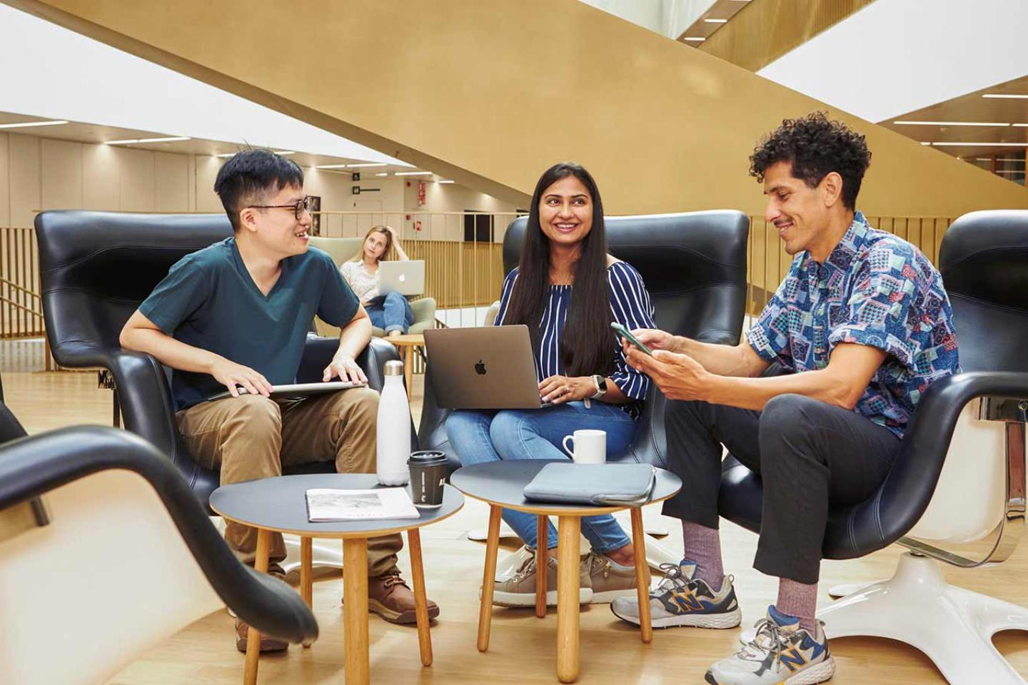 A group of smiling people sitting at a coffee table with laptops, having a meeting