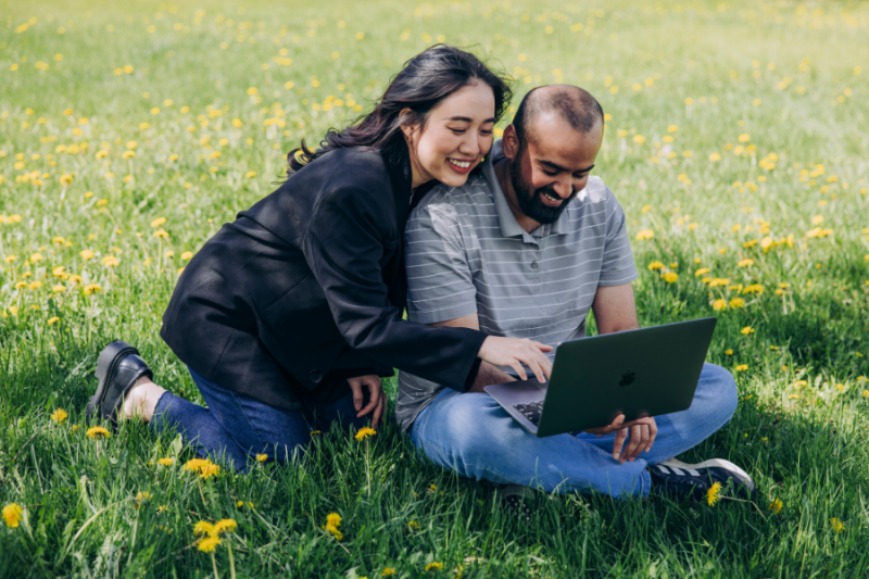 A pair of students on lawn, looking at laptop