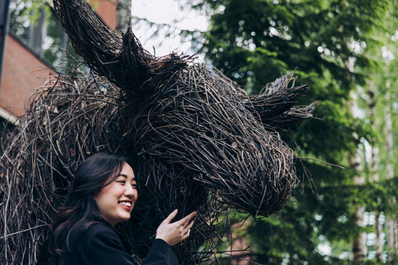 A female student with a moose sculpture made out of twigs