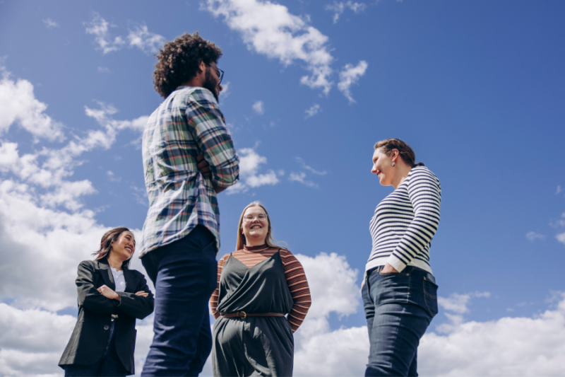 A group of students standing outdoors, against a blue sky with a few summer clouds