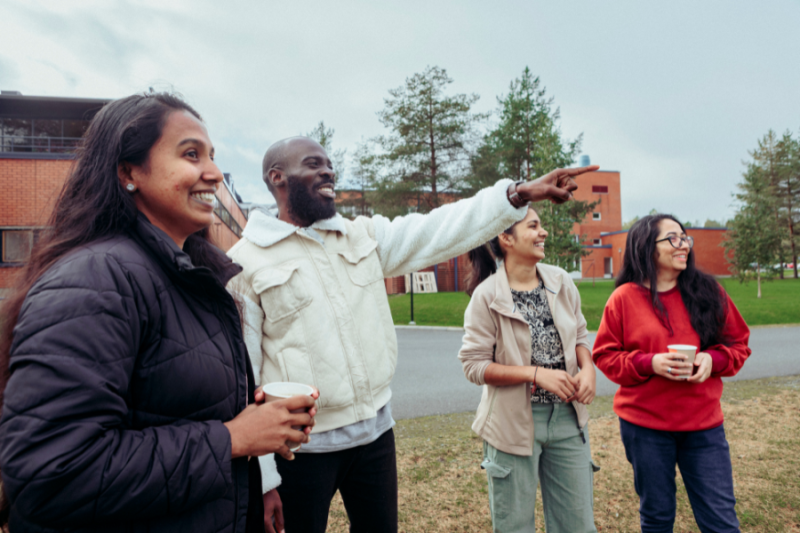 A group of international students on campus, outside and pointing at something in the distance